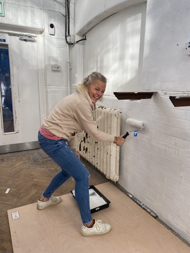 Head of Finance, Rachel, painting a white wall with a roller in hand, smiling 