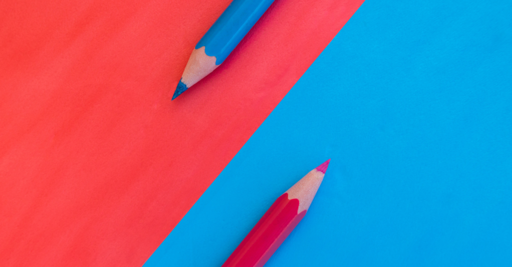 Two coloured pencils lie diagonally on contrasting red and blue backgrounds.